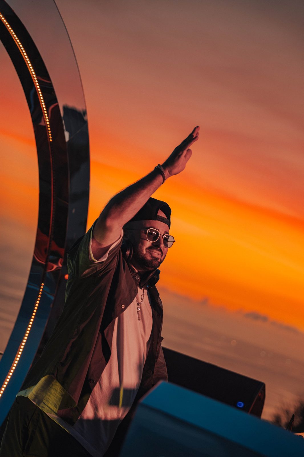 ERAN waving to the crowd from the booth under an orange sunset sky