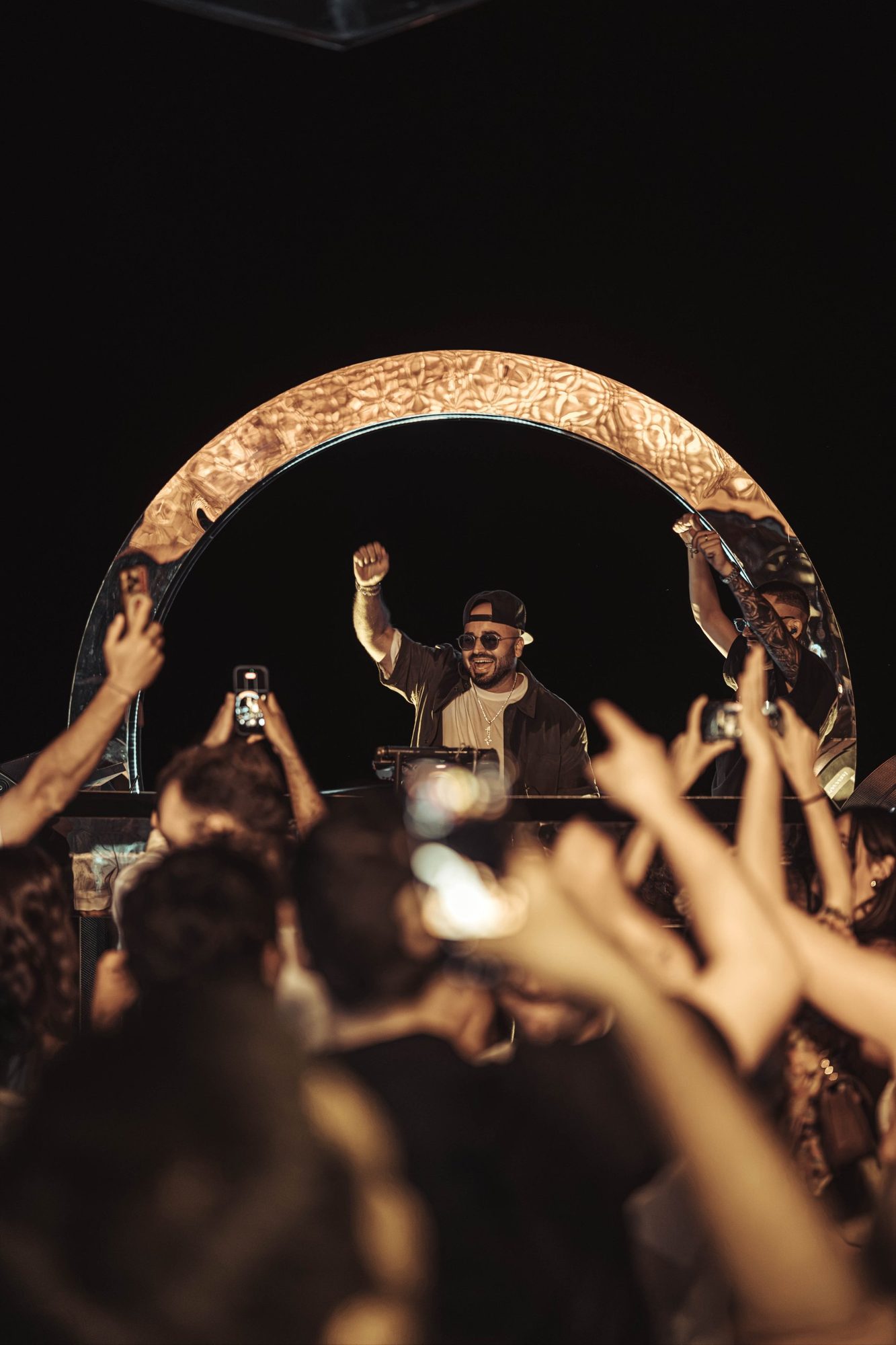 ERAN raising his fist inside a glowing arch above a crowd filming on their phones